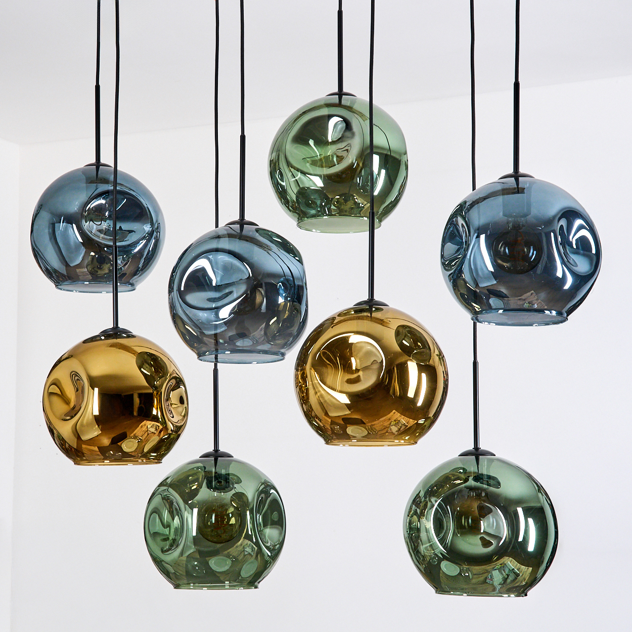 Acht Pendelleuchten mit kugelförmigen Glasschirmen in Blau, Grün und Gold hängen vor weißem Hintergrund.