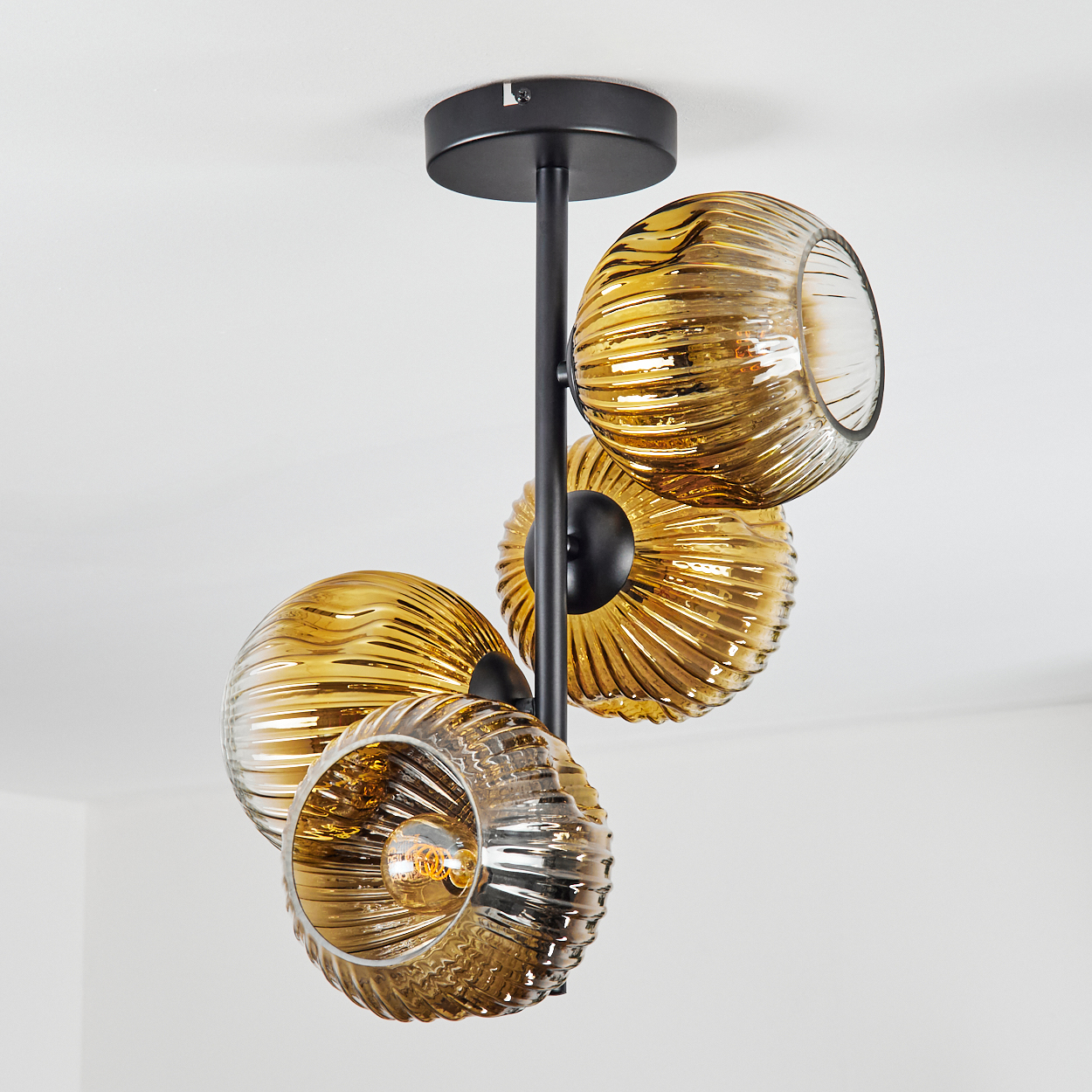 Eine moderne Deckenleuchte mit vier bernsteinfarbenen Glaskugelschirmen. Schwarze Metallstruktur vor weißer Decke.