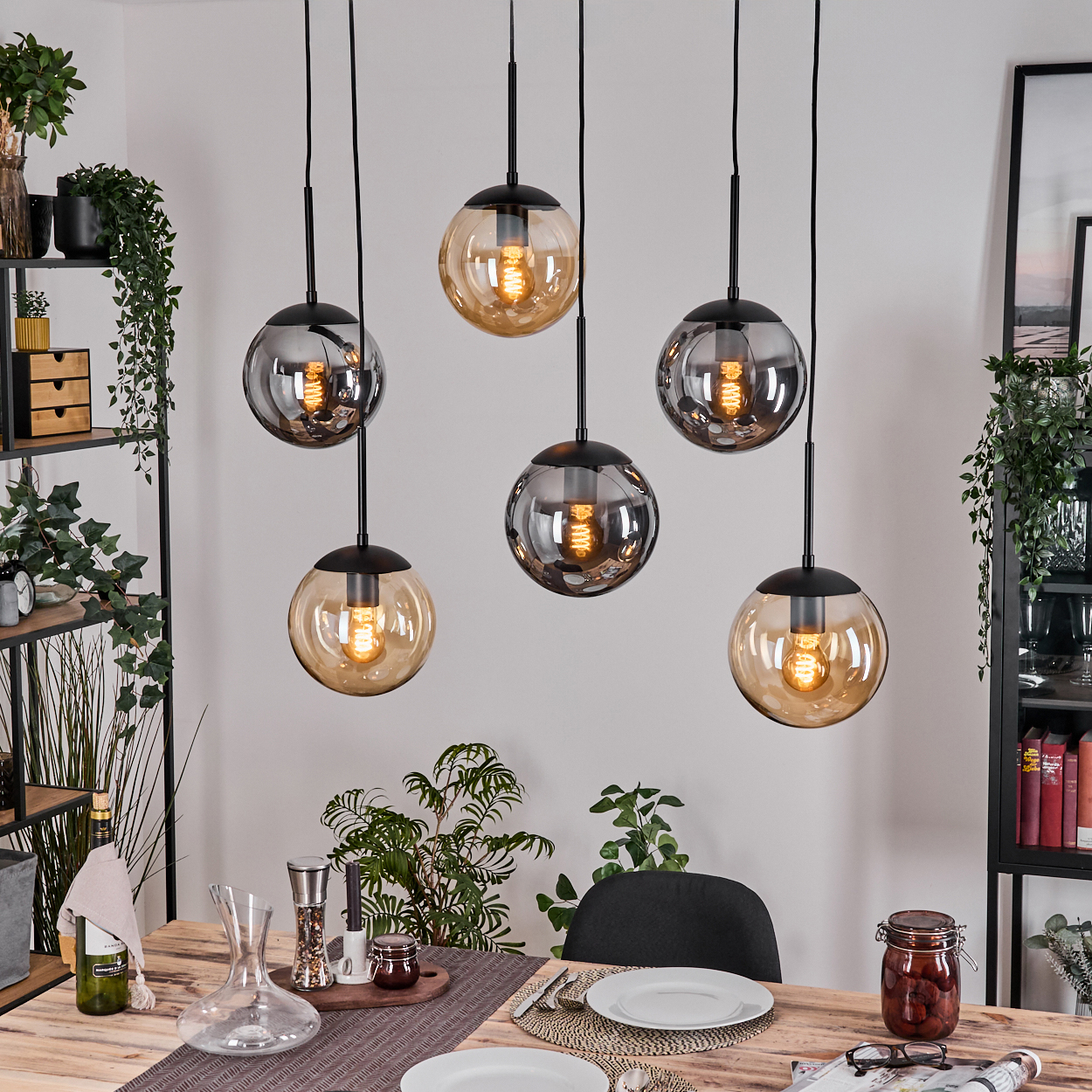 Esszimmer mit sechs hängenden Kugelleuchten. Holztisch für eine Mahlzeit gedeckt. Regale mit Pflanzen und Dekoration im Hintergrund.