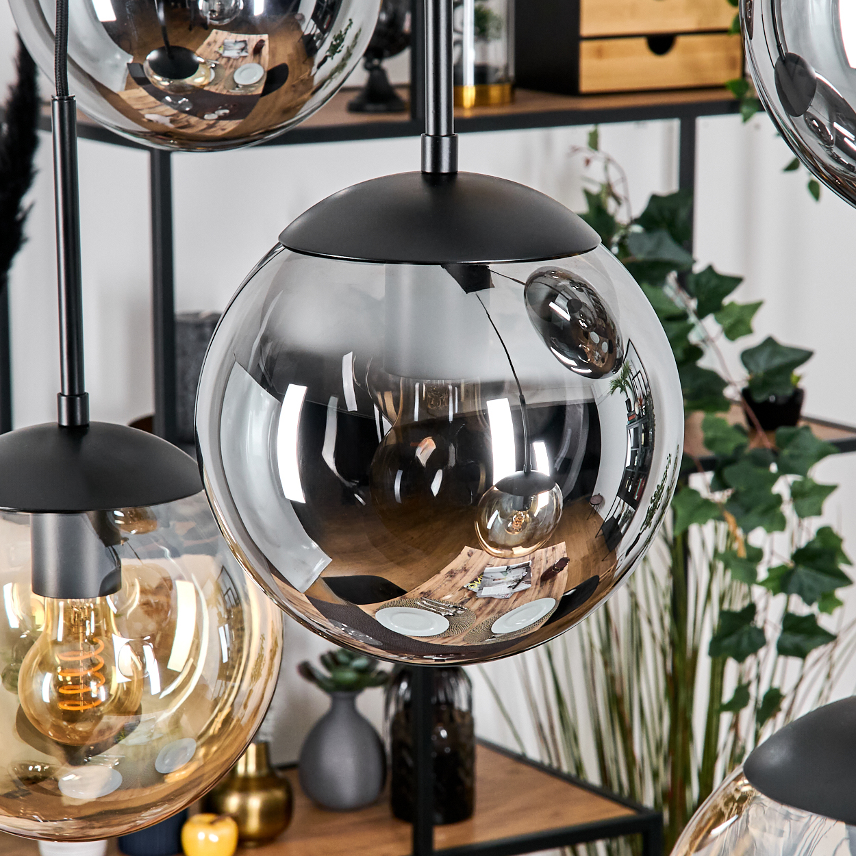 Nahaufnahme von modernen Pendelleuchten mit Glassphären, die den Raum reflektieren. Im Hintergrund sind Pflanzen und Vasen zu sehen.