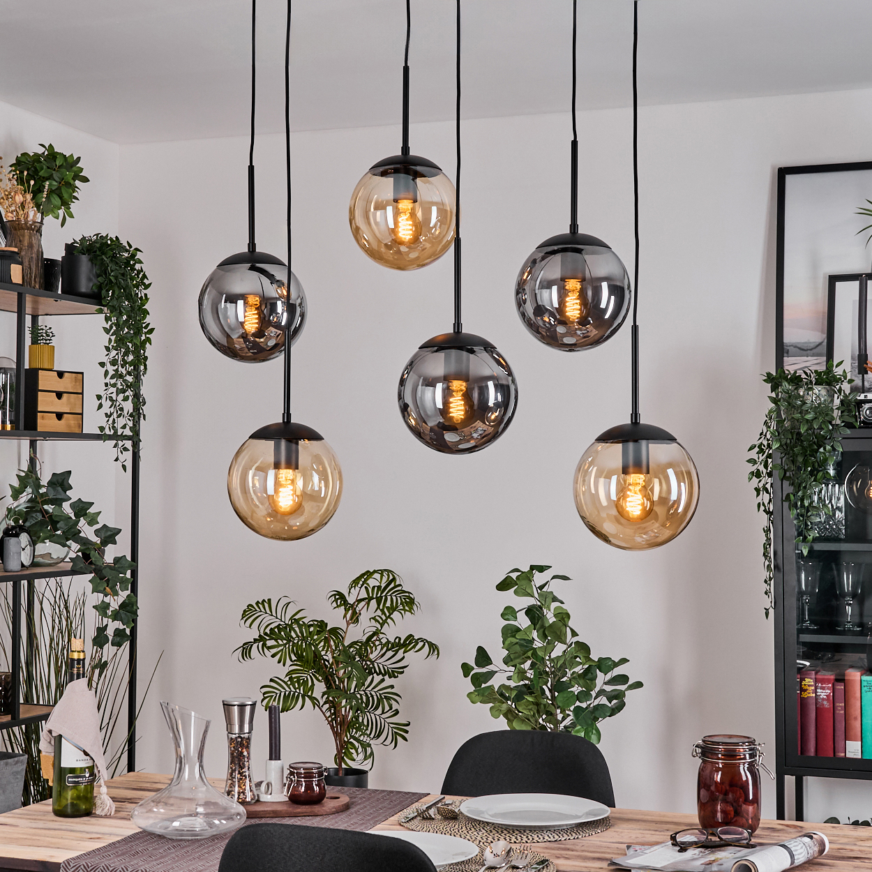 Esszimmer mit sechs hängenden Kugelleuchten. Tisch mit Pflanzen und Dekoration. Regale mit Pflanzen im Hintergrund.