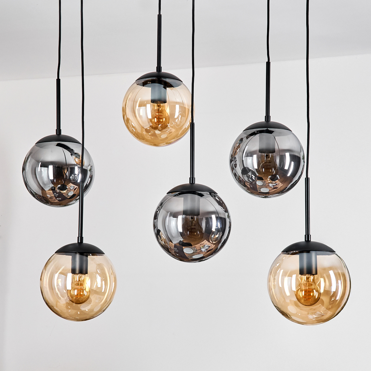 Sechs moderne Pendelleuchten. Einige sind klar, einige verspiegelt, alle kugelförmig. Schwarze Armaturen und Drähte vor weißer Wand.