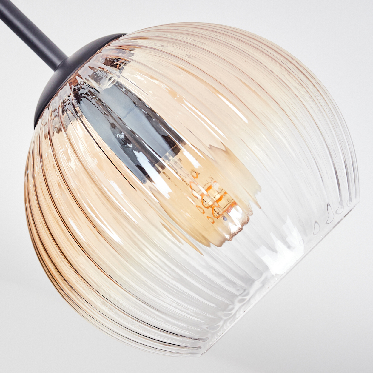Nahaufnahme einer Glasleuchte. Das Glas ist gerippt und hat einen bernsteinfarbenen Farbverlauf. Im Inneren befindet sich eine Glühbirne. Der Hintergrund ist weiß.