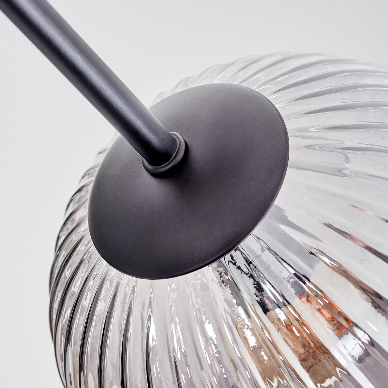 Nahaufnahme einer Glaslampe mit schwarzem Metallarm und -fuß. Das Glas ist gerippt und klar und reflektiert das Licht. Weißer Hintergrund.