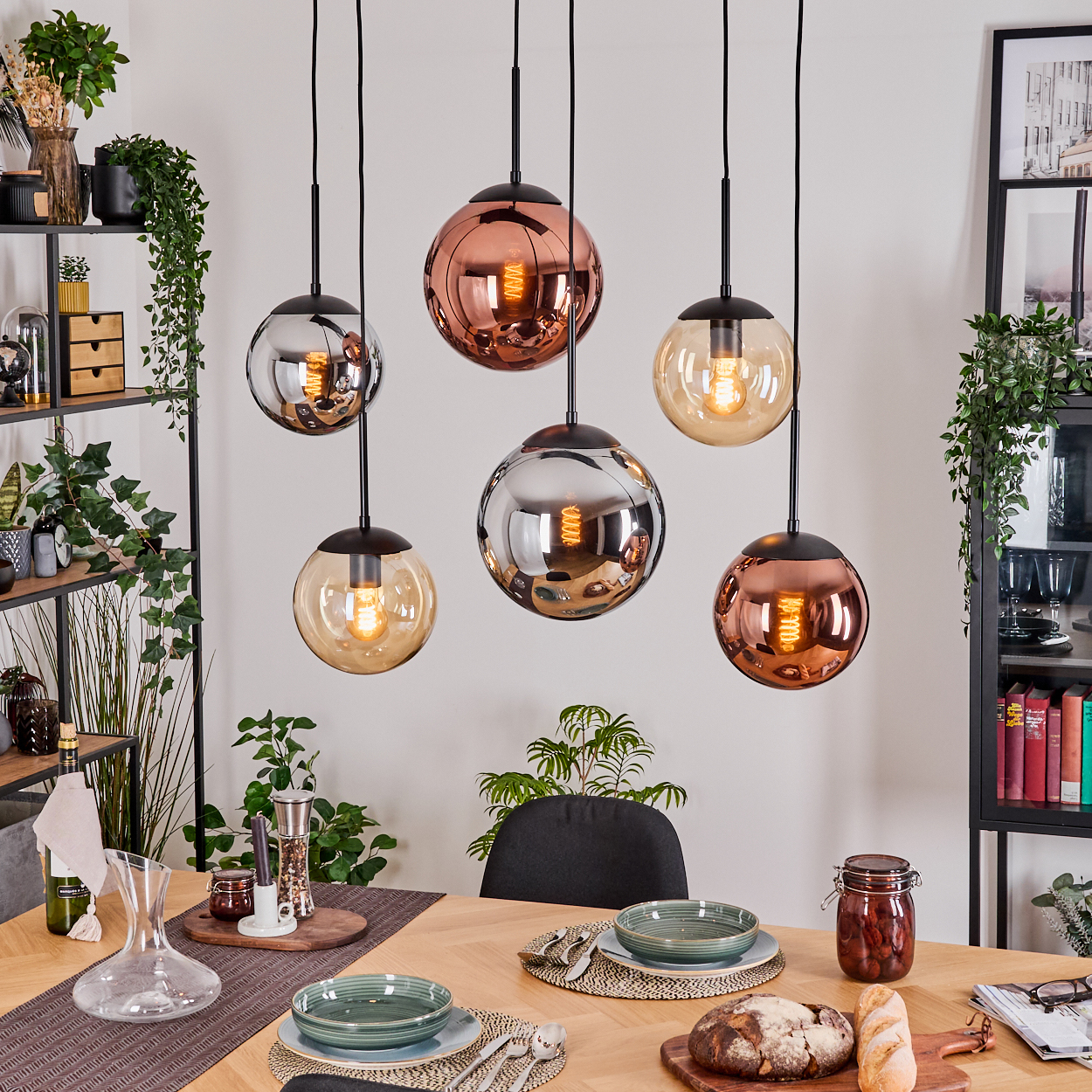 Esszimmer mit sechs Kugellampen. Tisch mit Schalen, Brot und Karaffe. Regale mit Pflanzen.