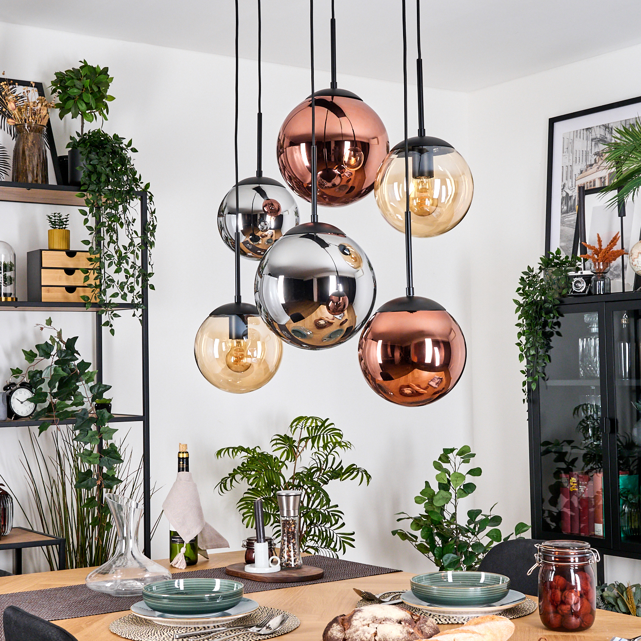 Esszimmer mit Pendelleuchten, gedecktem Tisch, Pflanzen und Schrank. Leuchten sind kupfer- und silberfarben. Tisch ist gedeckt.