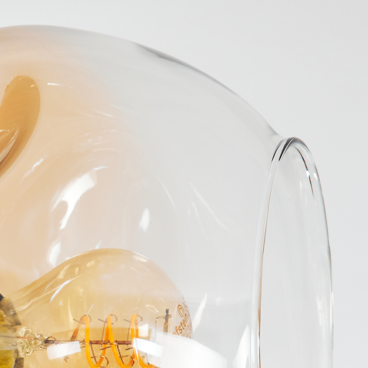 Nahaufnahme einer Glühbirne in einem Glaslampenschirm. Die Birne hat einen warmen, orangefarbenen Schein und der Schirm ist klar.