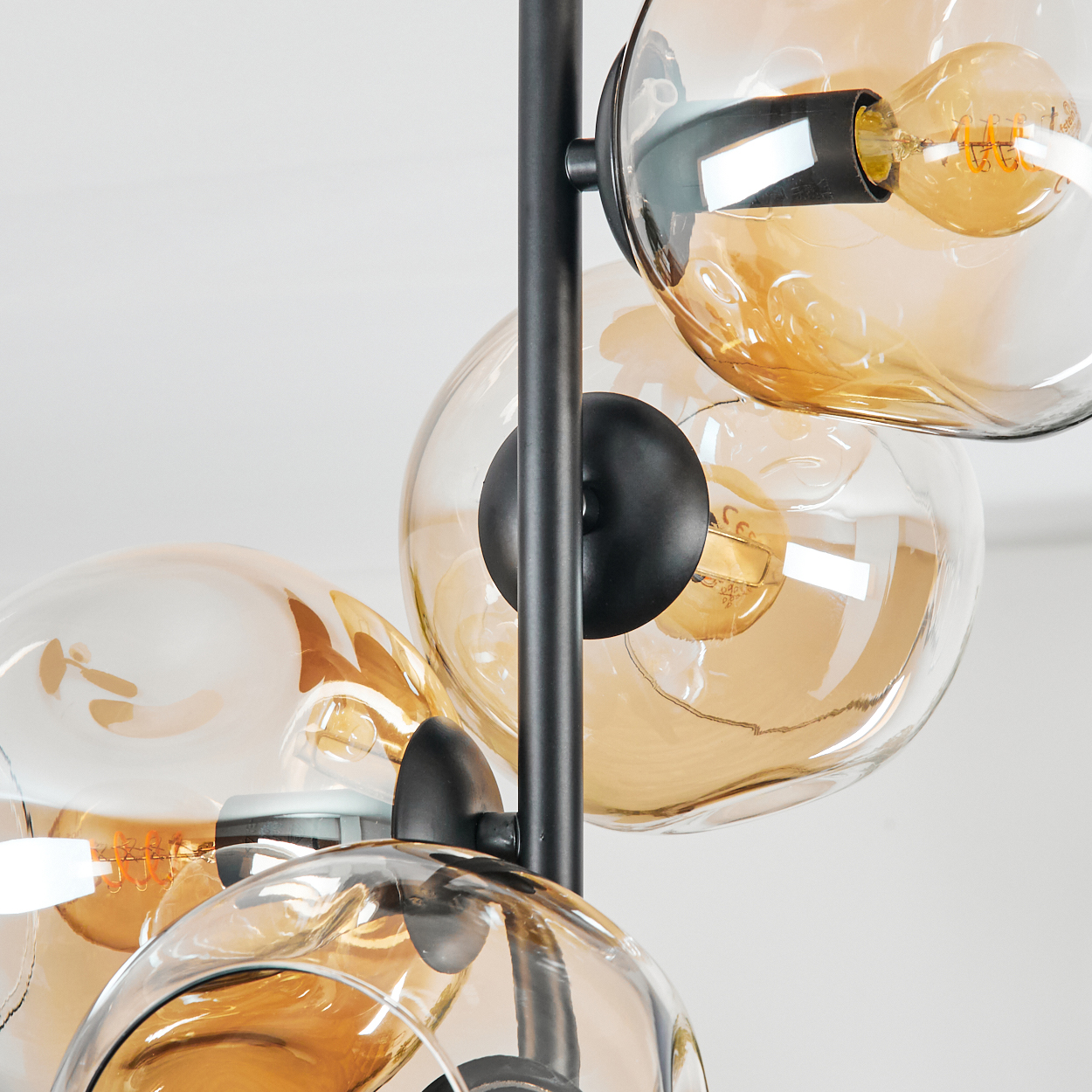 Nahaufnahme einer modernen Deckenleuchte. Sie hat schwarze Stäbe und mehrere Glaskugeln mit bernsteinfarbenem Glas. Der Hintergrund ist weiß.