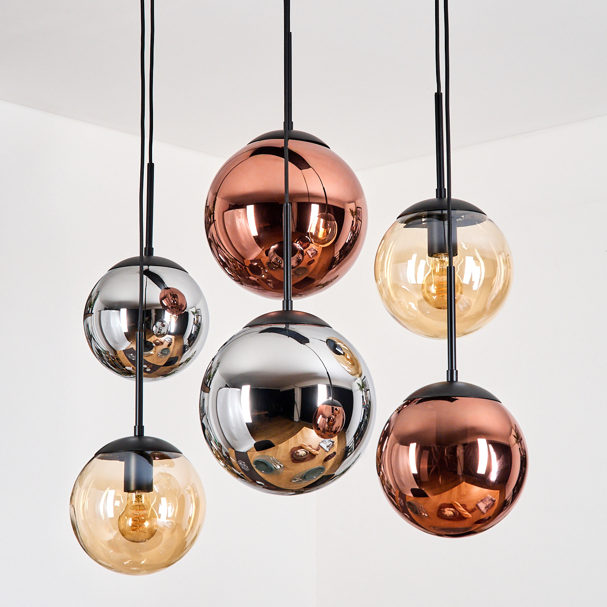 Sechs moderne Pendelleuchten. Kugelförmige Schirme aus Kupfer, Silber und Amberglas. Schwarze Stiele und Deckenbefestigungen. Weißer Hintergrund.