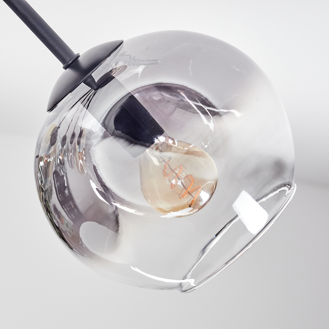 Moderne Glasleuchte mit schwarzem Stiel. Im Inneren des Glases ist eine Glühbirne sichtbar. Der Hintergrund ist eine weiße Decke.