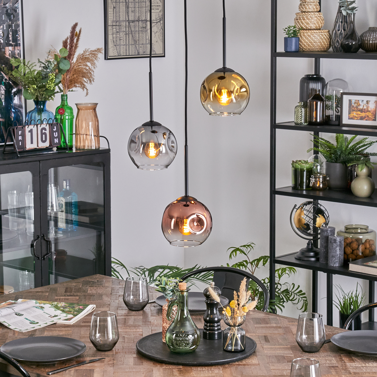 Esszimmer mit Holztisch, Hängelampen und Dekoration. Enthält Teller, Gläser und ein schwarzes Regal.