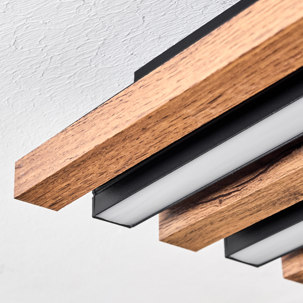 Nahaufnahme einer Deckenleuchte. Sie verfügt über Holzbalken mit schwarzen Halterungen und weiße LED-Leuchten. Die Decke ist weiß.