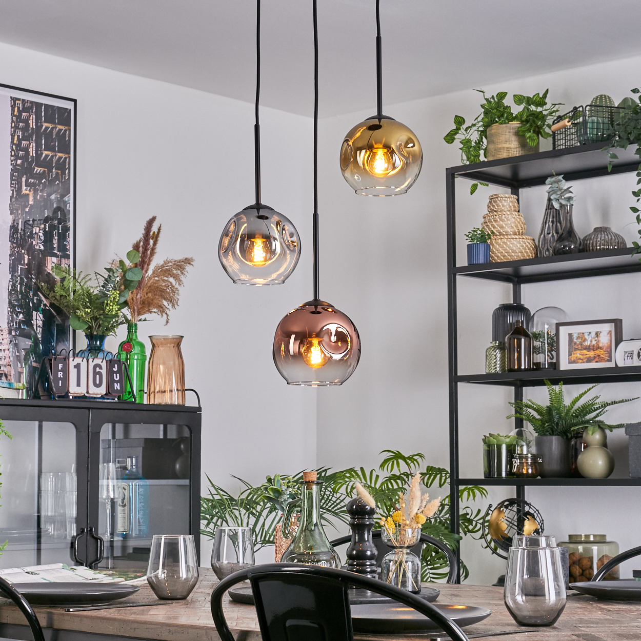 Esszimmer mit drei Hängelampen. Tisch mit Gläsern und Tellern. Regale mit Pflanzen und Deko im Hintergrund.