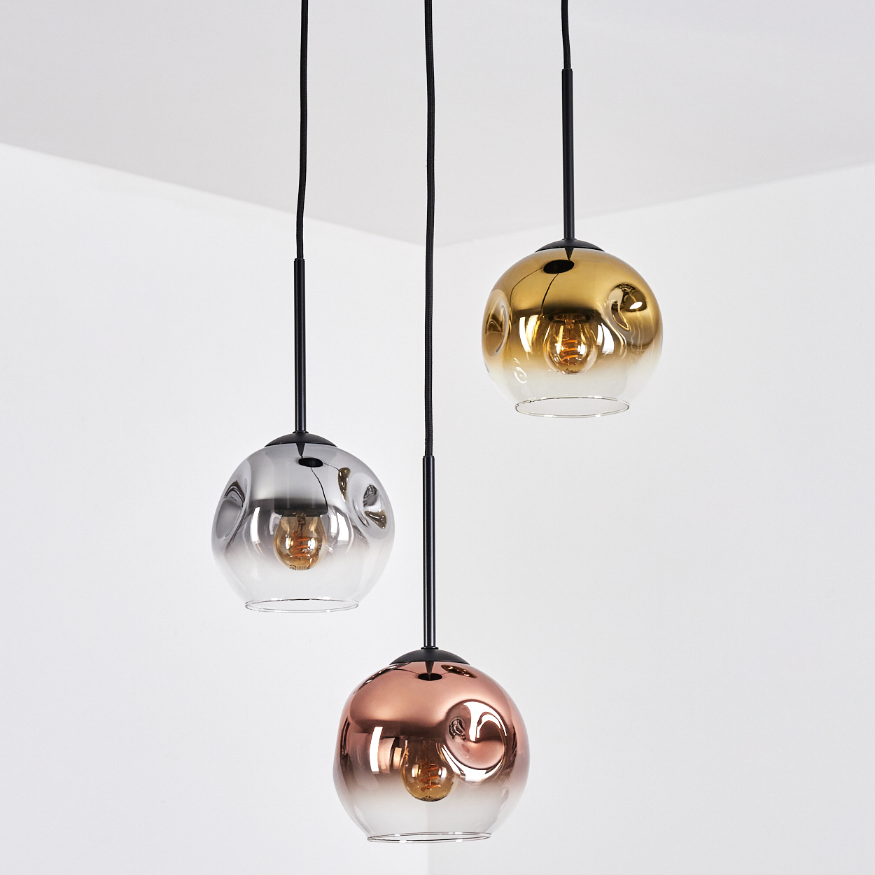 Drei Pendelleuchten mit kugelförmigen Glasschirmen in Silber, Gold und Kupfer. Jede hat ein schwarzes Kabel und eine sichtbare Glühbirne.