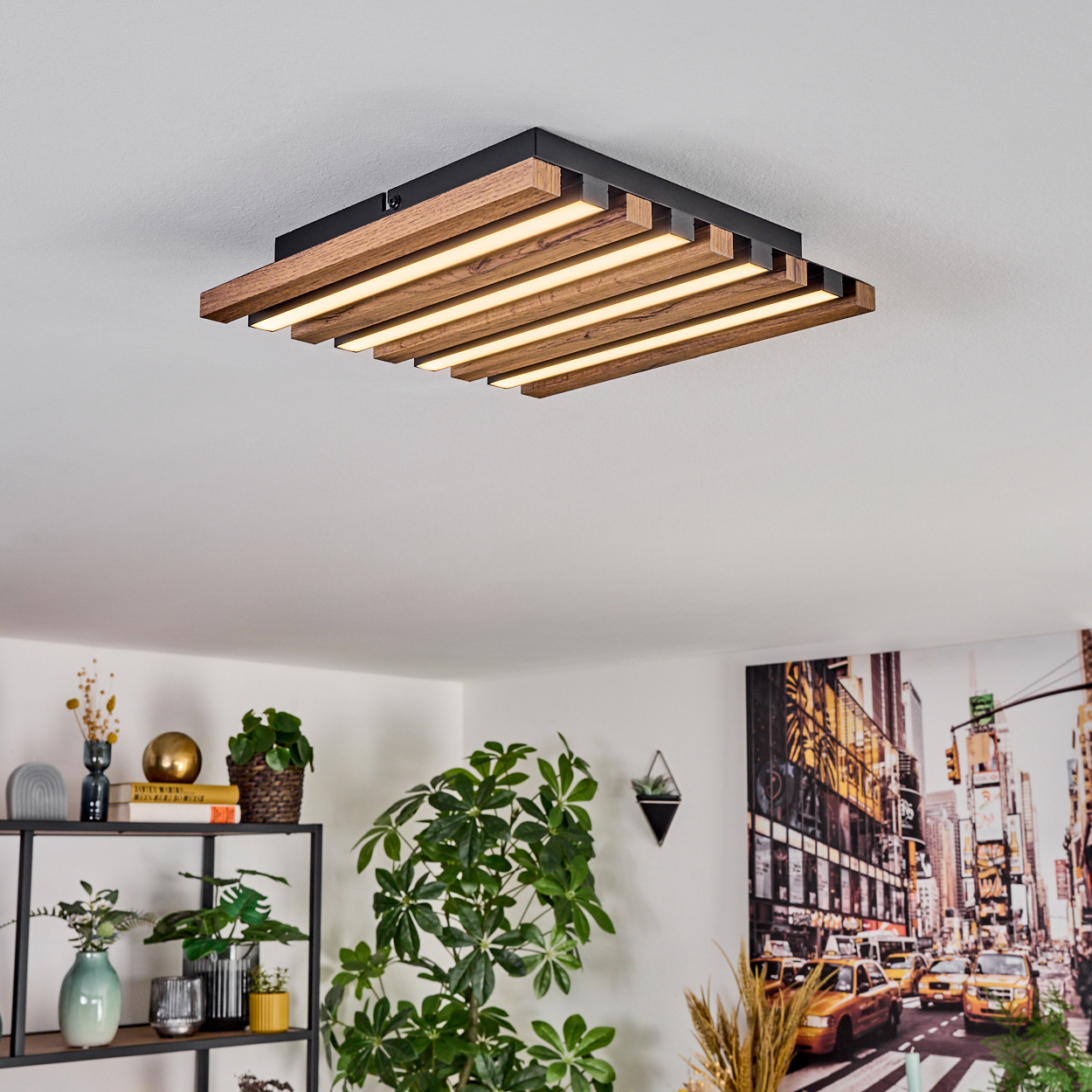Eine moderne Deckenleuchte mit Holzlatten und integrierten Lichtern. Pflanzen und ein Regal mit Dekoration sind im Raum. Ein Gemälde der Skyline von New York ist an der Wand.