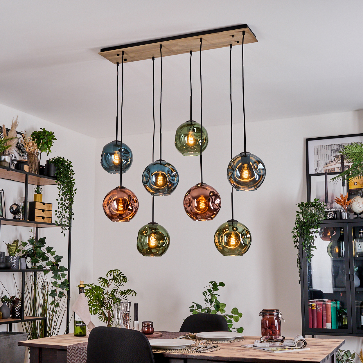 Esszimmer mit Holztisch, Hängelampen mit farbigen Glaskugeln und Zierpflanzen. Rechts ein gerahmtes Bild.