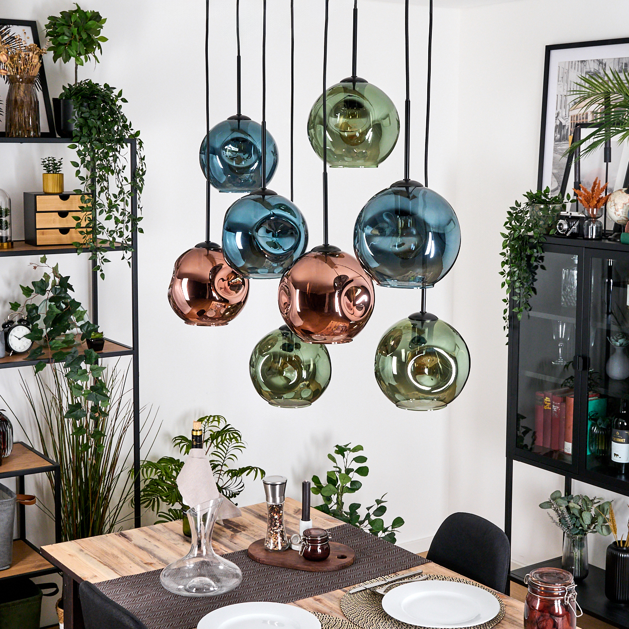 Ein Esszimmer mit hängenden Glaskugelleuchten. Ein Holztisch ist mit Tellern und einer Karaffe gedeckt. Regale mit Pflanzen und Dekor sind sichtbar.
