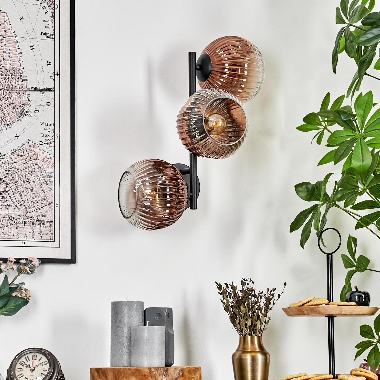 Eine Wandlampe mit drei Glaskugeln. Eine Karte, Kerzen und ein mehrstöckiges Tablett mit Keksen und einem kleinen Kürbis sind ebenfalls im Bild.