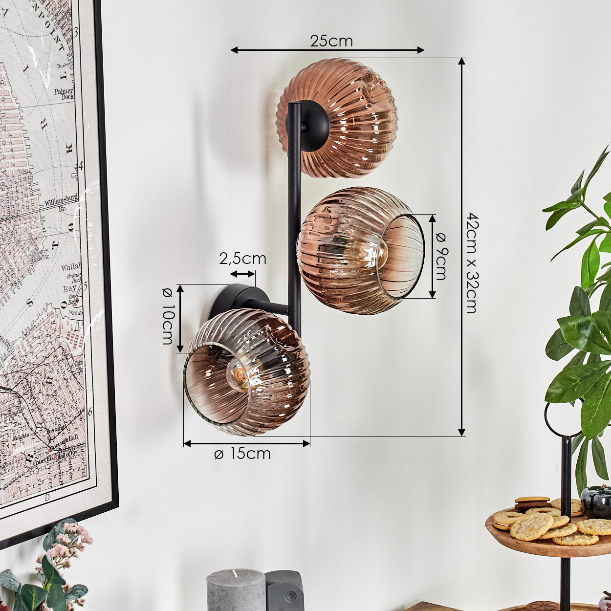 Eine Wandlampe mit drei Glasschirmen. Die Schirme sind bernsteinfarben und gerippt. Eine Karte und eine Pflanze sind in der Nähe.
