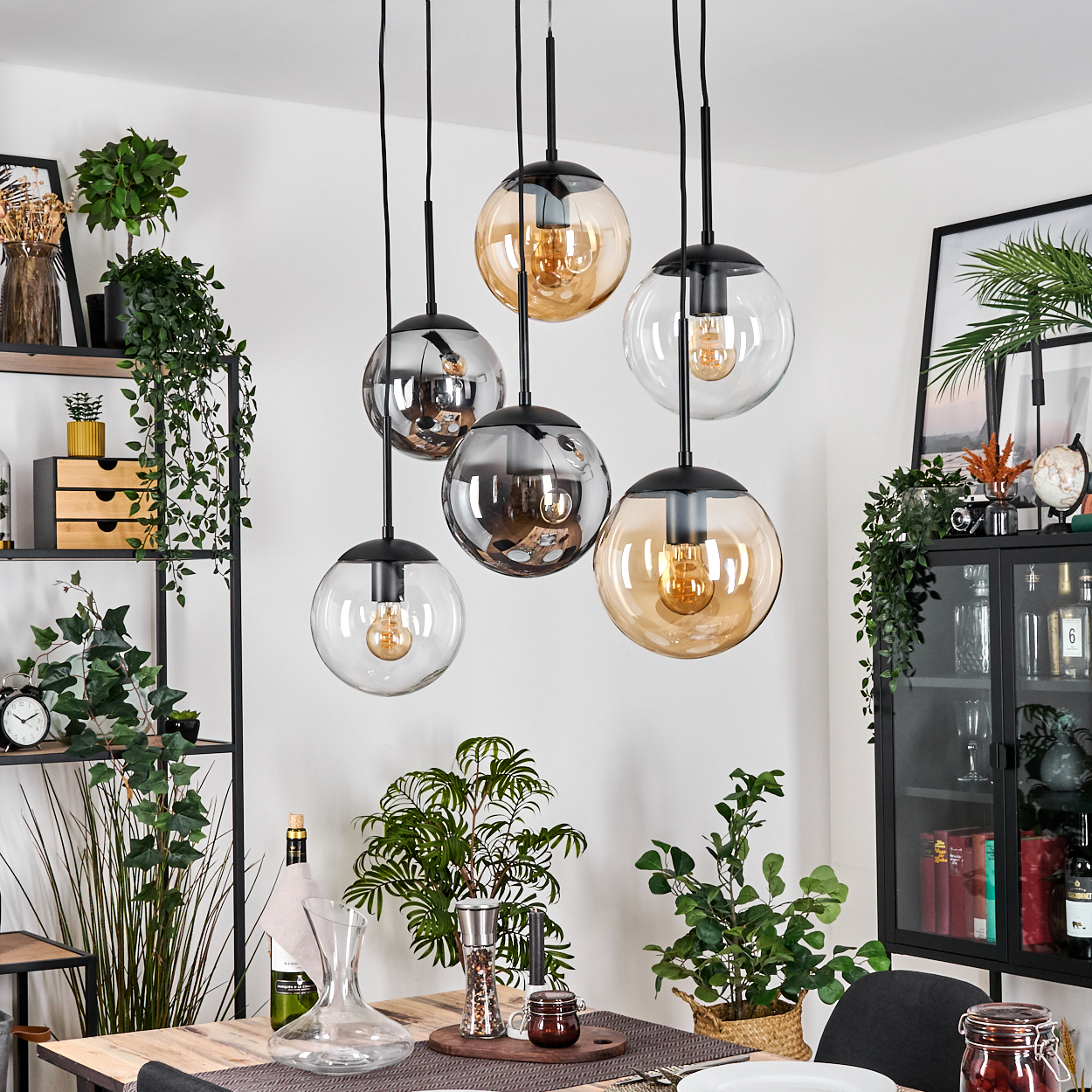 Esszimmer mit hängenden Kugelleuchten. Tisch mit Pflanzen und Dekoration. Pflanzen und Regale mit Dekoration im Hintergrund.