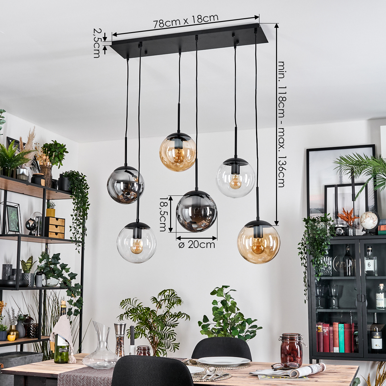 Ein Esszimmer mit einem schwarzen Kronleuchter mit Glaskugeln, Pflanzen, einem Holztisch mit Tellern und einem schwarzen Schrank.