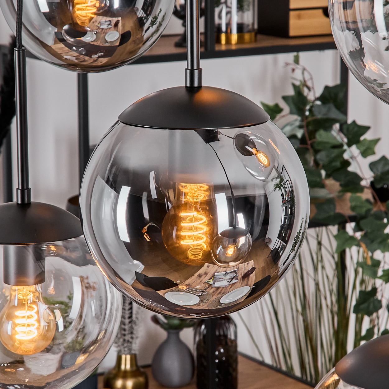 Nahaufnahme einer modernen Hängelampe mit kugelförmigen Glasschirmen. Jeder enthält eine leuchtende, spiralförmige Glühbirne, die die Umgebung reflektiert.