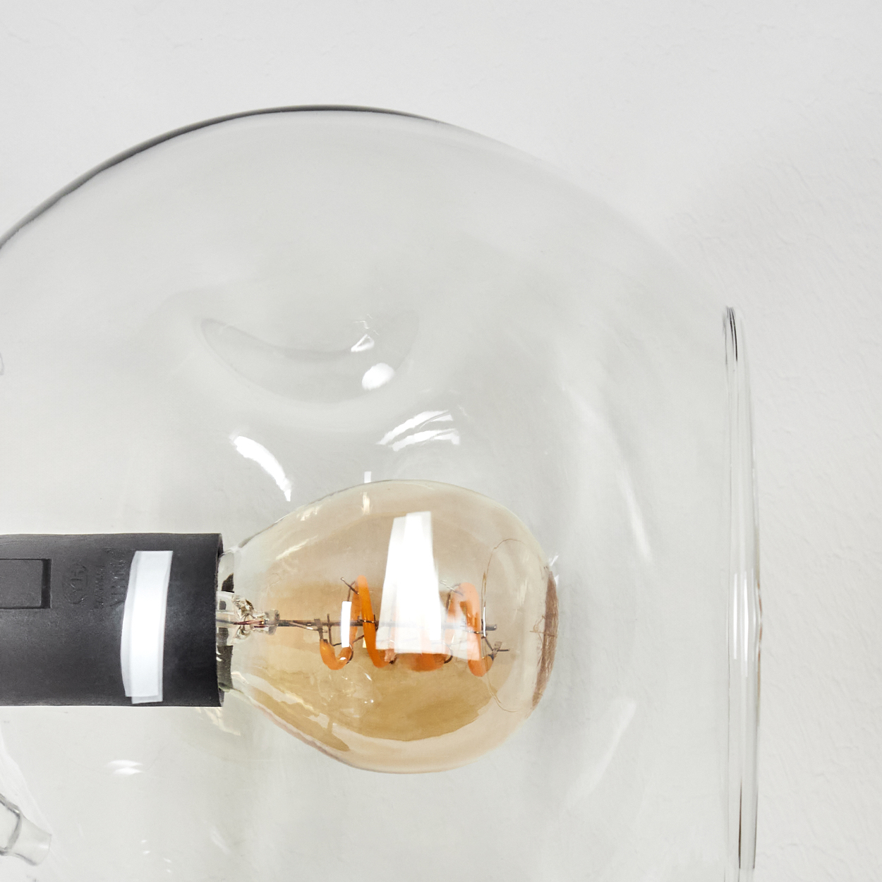 Nahaufnahme einer Glühbirne in einem Glasgehäuse. Die Glühbirne leuchtet, mit sichtbaren Filamenten. Das Gehäuse hat eine klare, runde Form.