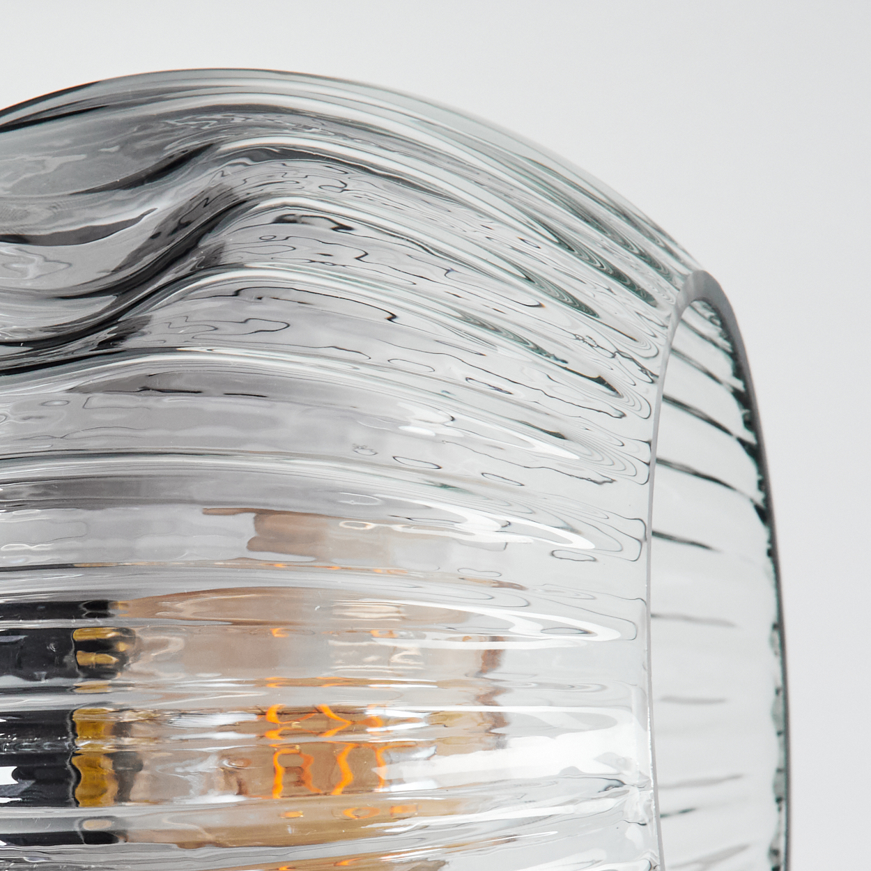 Nahaufnahme eines Lampenschirms aus Glas mit gewölbtem, geriffeltem Design. Eine Glühbirne ist sichtbar. Der Hintergrund ist weiß.