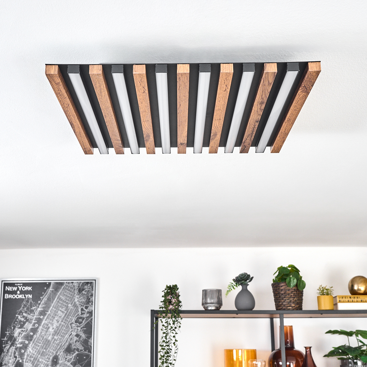 Moderne Deckenleuchte mit Holz- und weißen Paneelen. Darunter Regale mit Pflanzen und Dekoration vor weißer Wand.