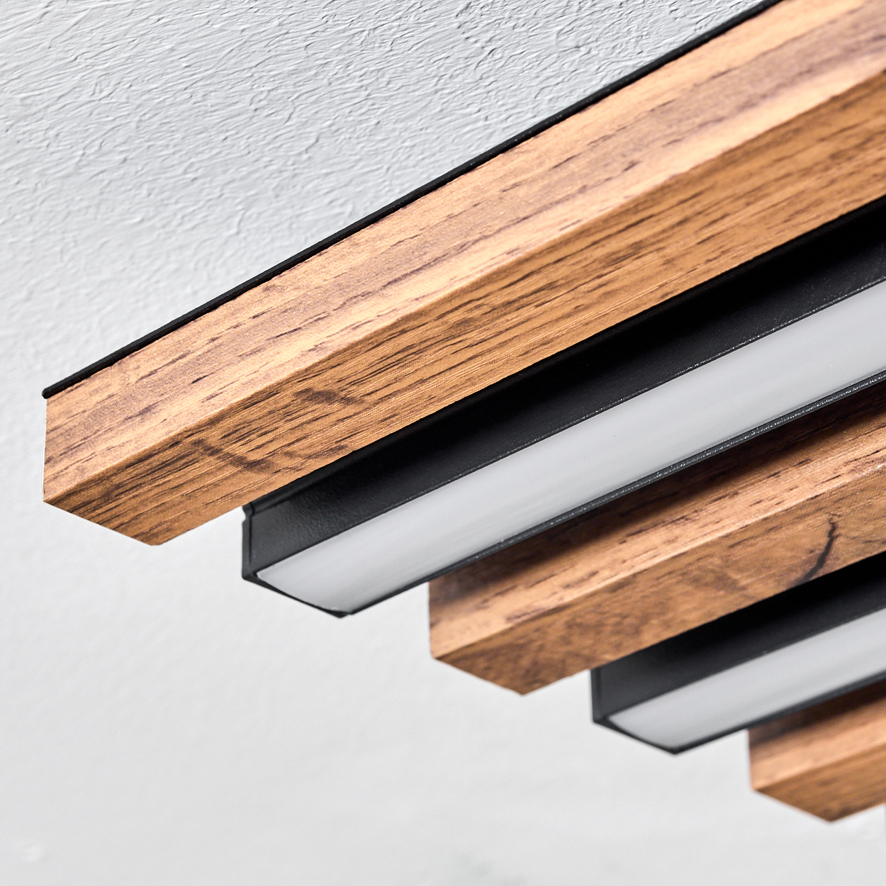 Nahaufnahme einer Deckenleuchte mit Holzbalken und weißen Lichtstreifen. Der Hintergrund ist eine weiß strukturierte Decke.