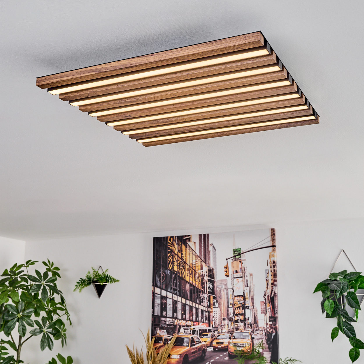 Eine rechteckige Deckenlampe aus Holz mit integrierten Lichtern. Darunter ein Stadtbildgemälde und Topfpflanzen.