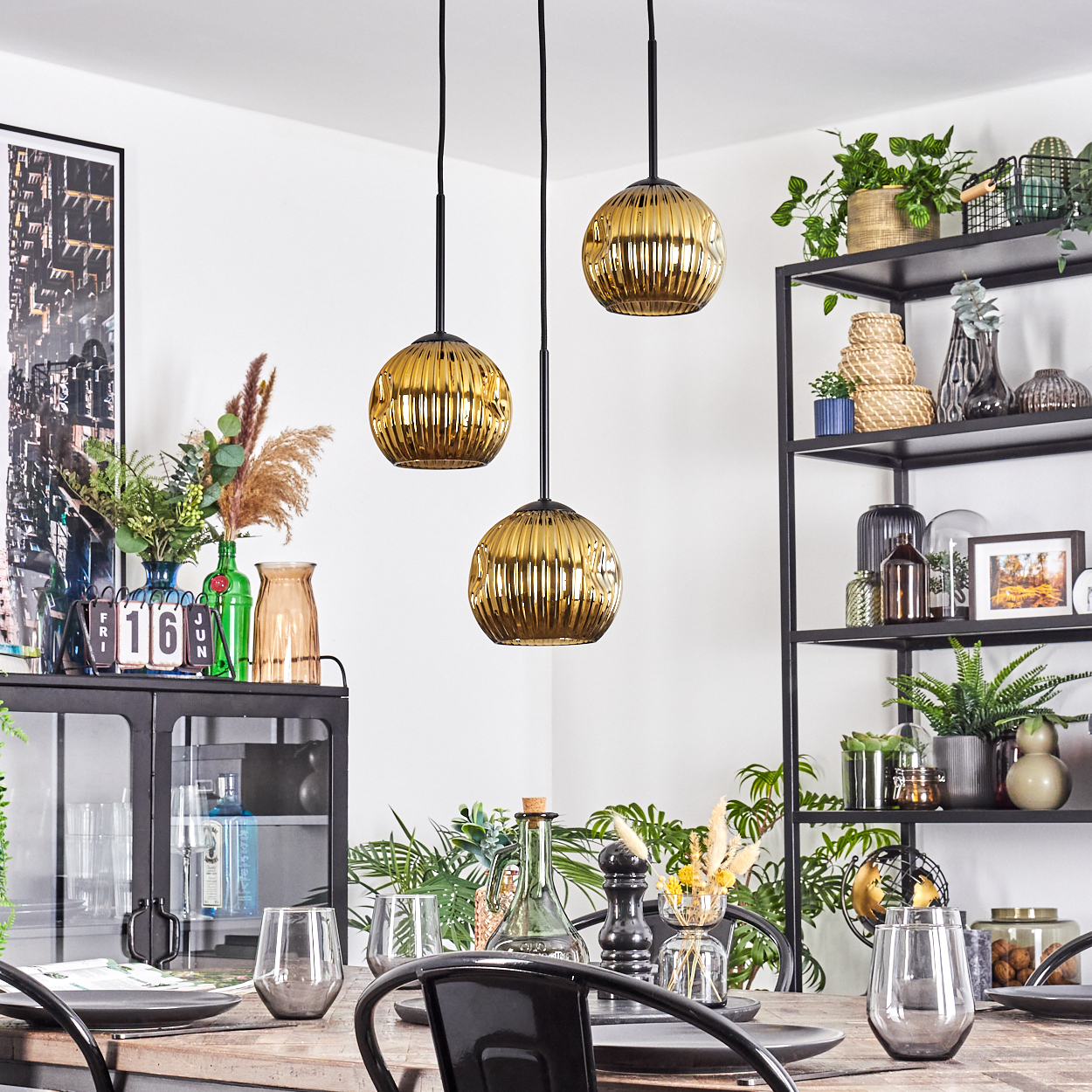 Esszimmer mit goldenen Hängelampen, Tischdeko und schwarzen Metallregalen mit Pflanzen und Dekoration.