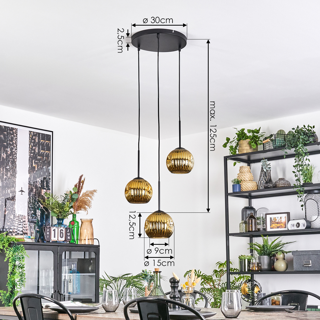 Drei goldene Pendelleuchten hängen von der Decke. Ein Esstisch mit Dekoration und ein Regal mit Pflanzen sind sichtbar.