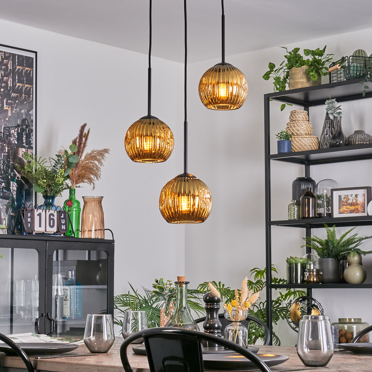 Esszimmer mit drei goldenen Pendelleuchten, einem gedeckten Tisch und einem schwarzen Regal.