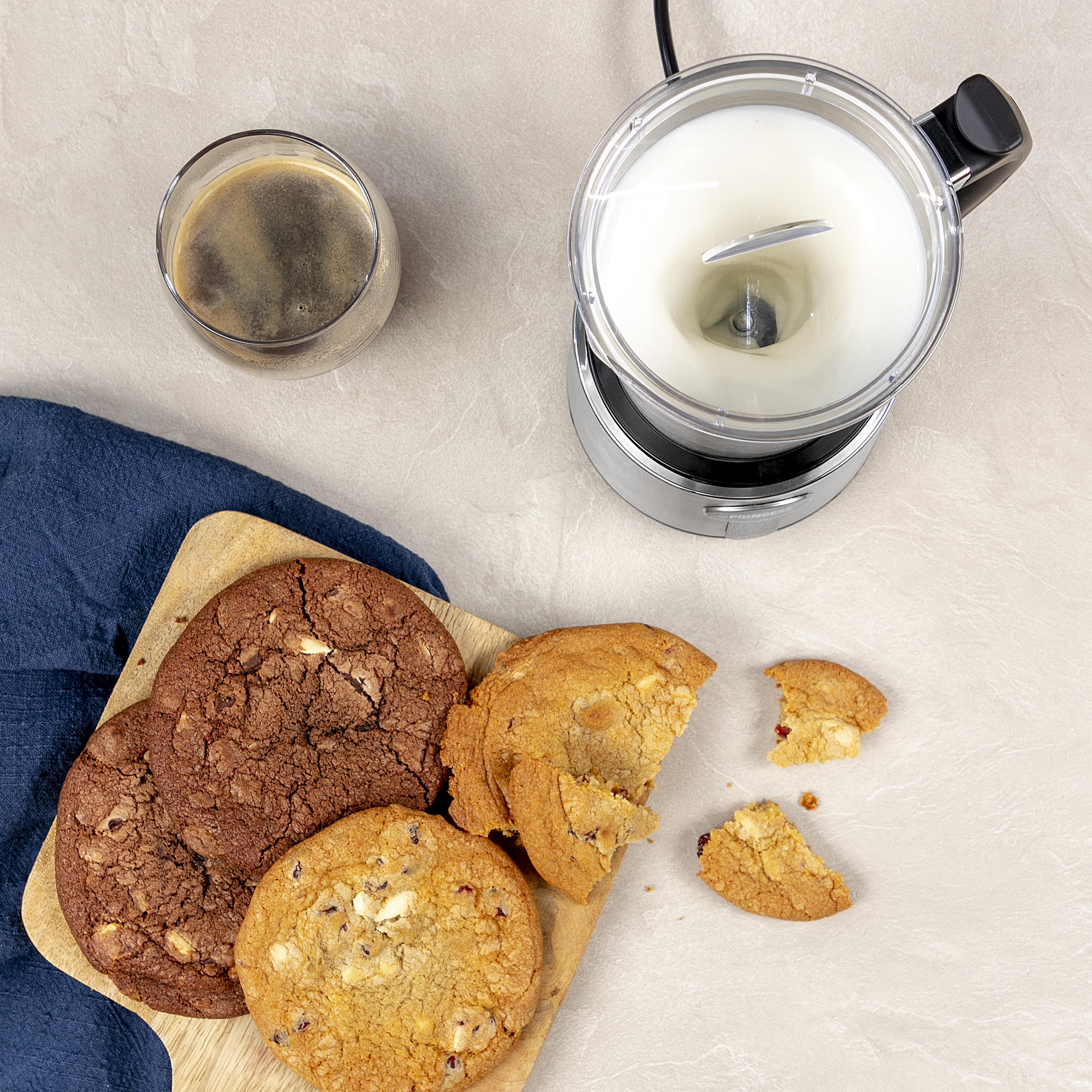 Widok z góry na ciastka, napój kawowy i spieniacz do mleka na jasnej powierzchni.