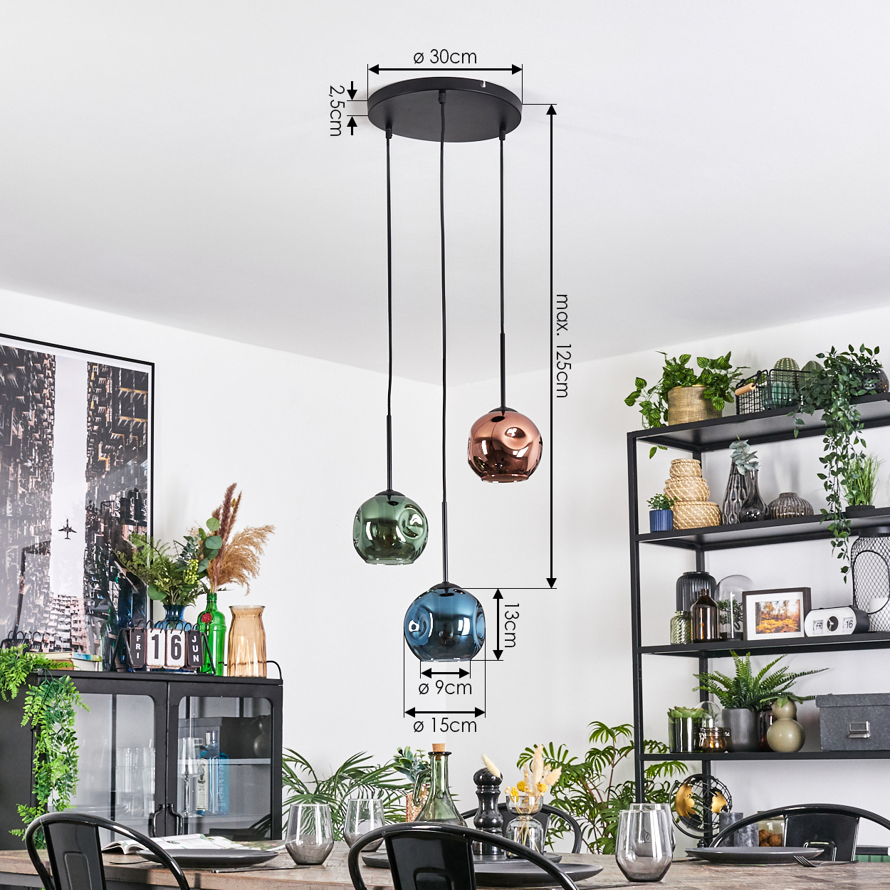 Drei Pendelleuchten mit Glaskugeln hängen von der Decke. Ein Esstisch ist mit Gläsern gedeckt und ein schwarzes Metallregal mit Pflanzen.