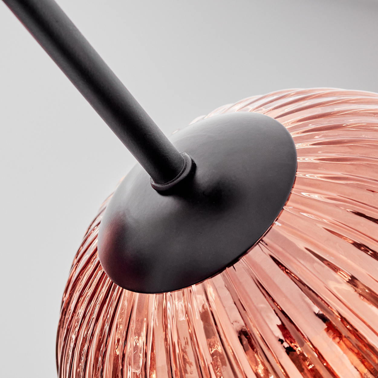 Nahaufnahme einer Leuchte. Sie hat einen bronzefarbenen Glasschirm mit geripptem Design, schwarzen Träger und einen hellen Hintergrund.