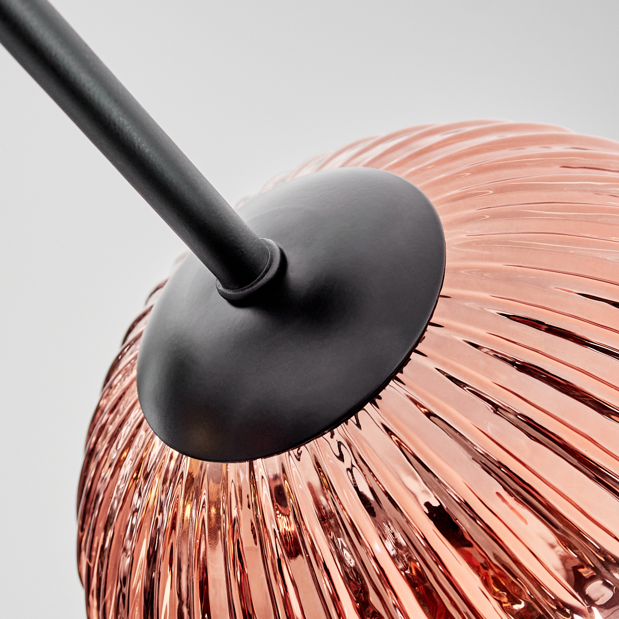 Nahaufnahme eines kupferfarbenen Glasschirms mit schwarzem Metallträger. Der Schirm hat eine gerippte Textur und wird von innen beleuchtet.