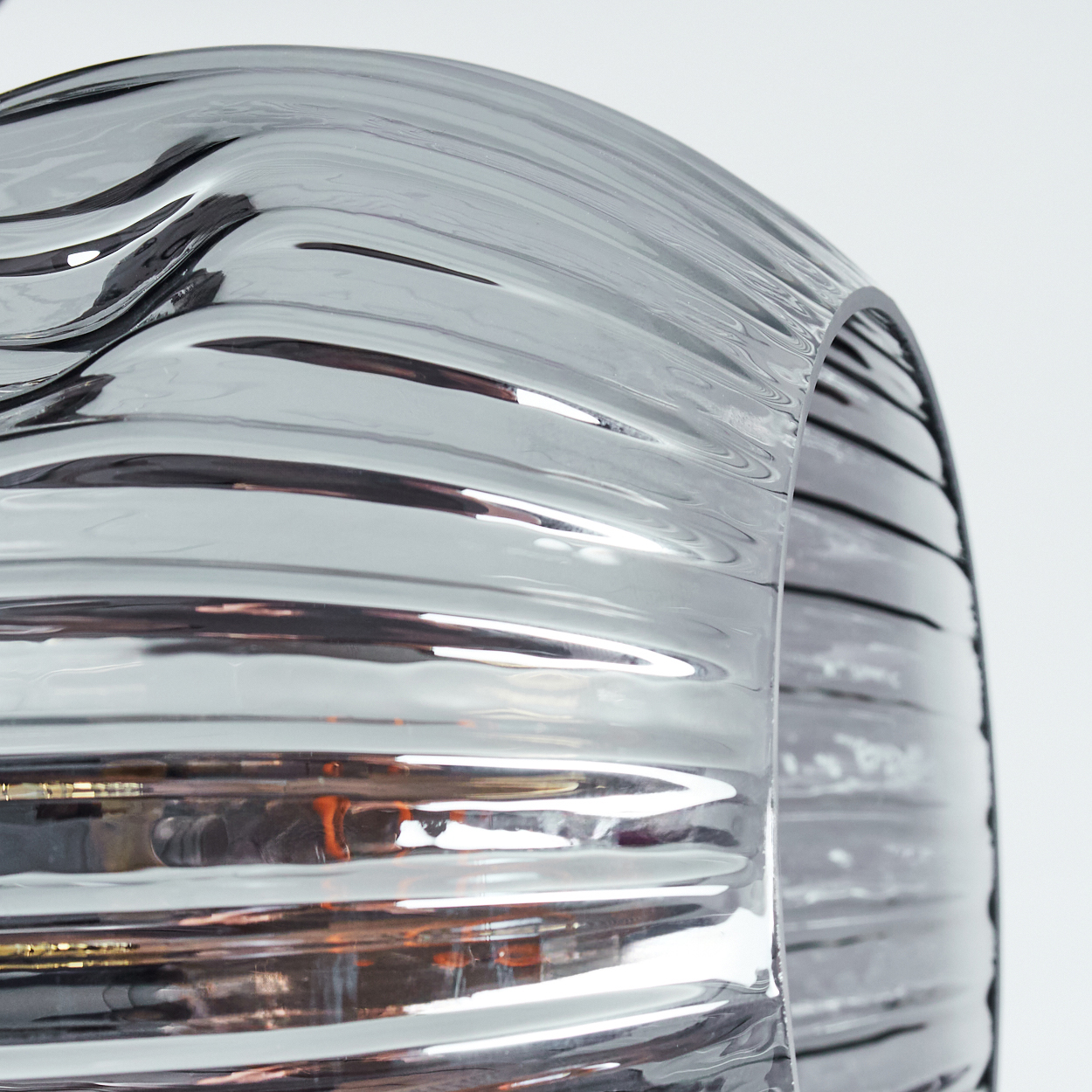 Nahaufnahme eines gebogenen, transparenten, gerippten Glasobjekts. Das Glas hat reflektierende Oberflächen und reflektiert Licht und Hintergrund.