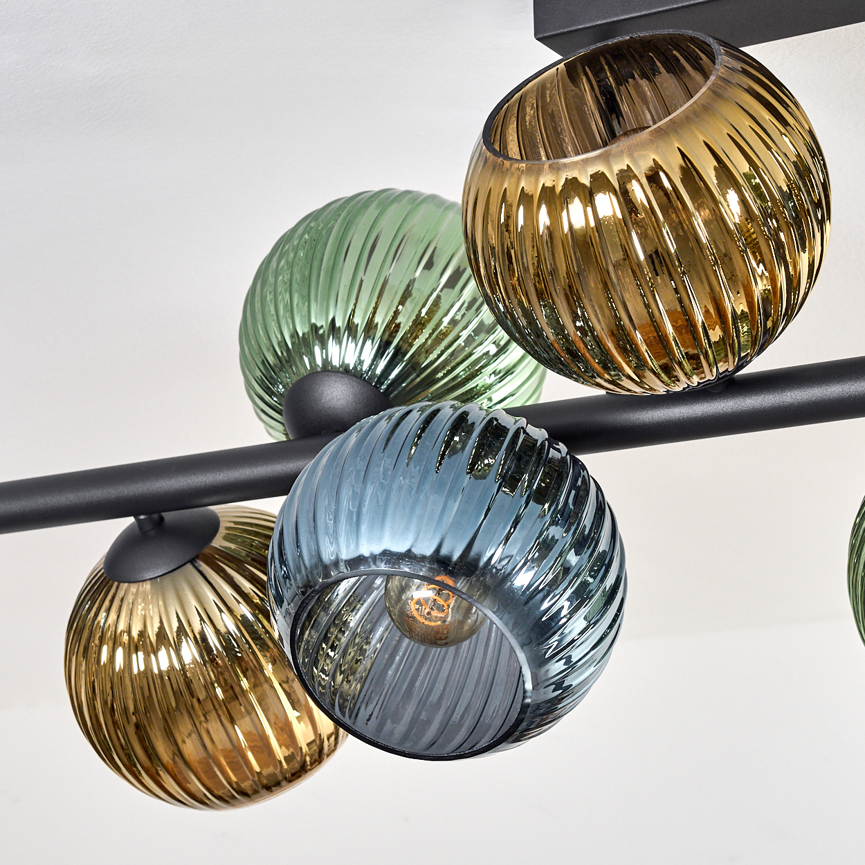 Eine moderne Deckenleuchte mit mehreren Glaskugeln in Grün, Gold und Blau, montiert auf einem schwarzen Metallrahmen.
