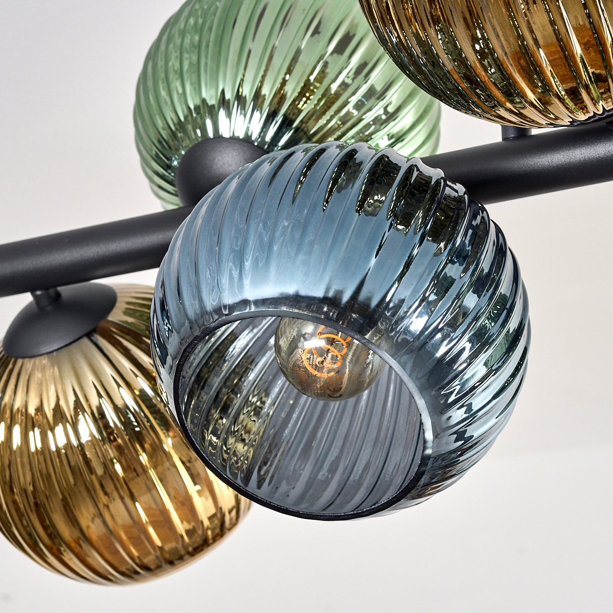 Nahaufnahme einer modernen Deckenleuchte mit farbigen Glaskugeln. Blaue, grüne und goldene Glasschirme mit schwarzem Metallrahmen.
