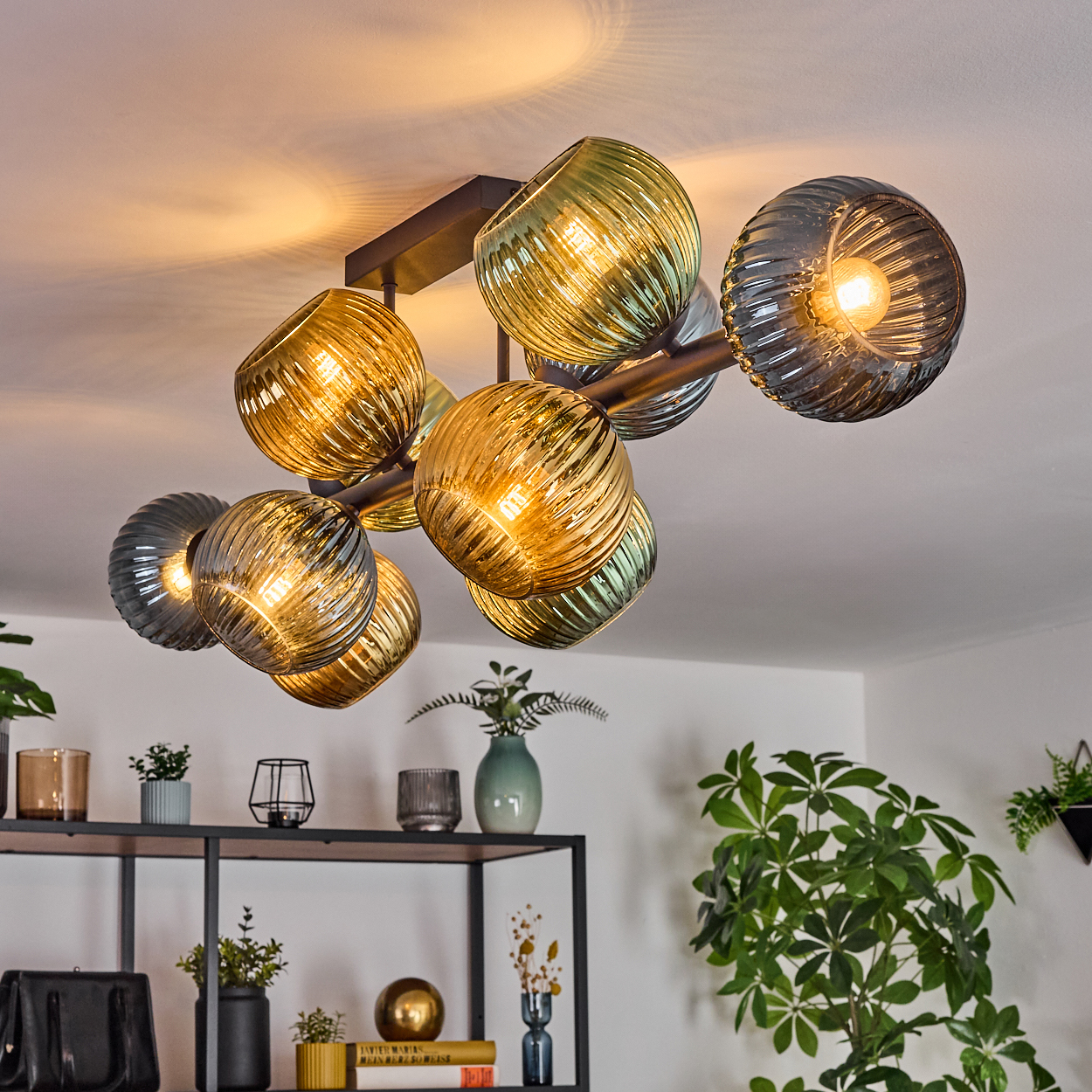 Eine moderne Deckenleuchte mit Glaskugeln in verschiedenen Farben beleuchtet den Raum. Darunter ein Regal mit Deko und Pflanzen.
