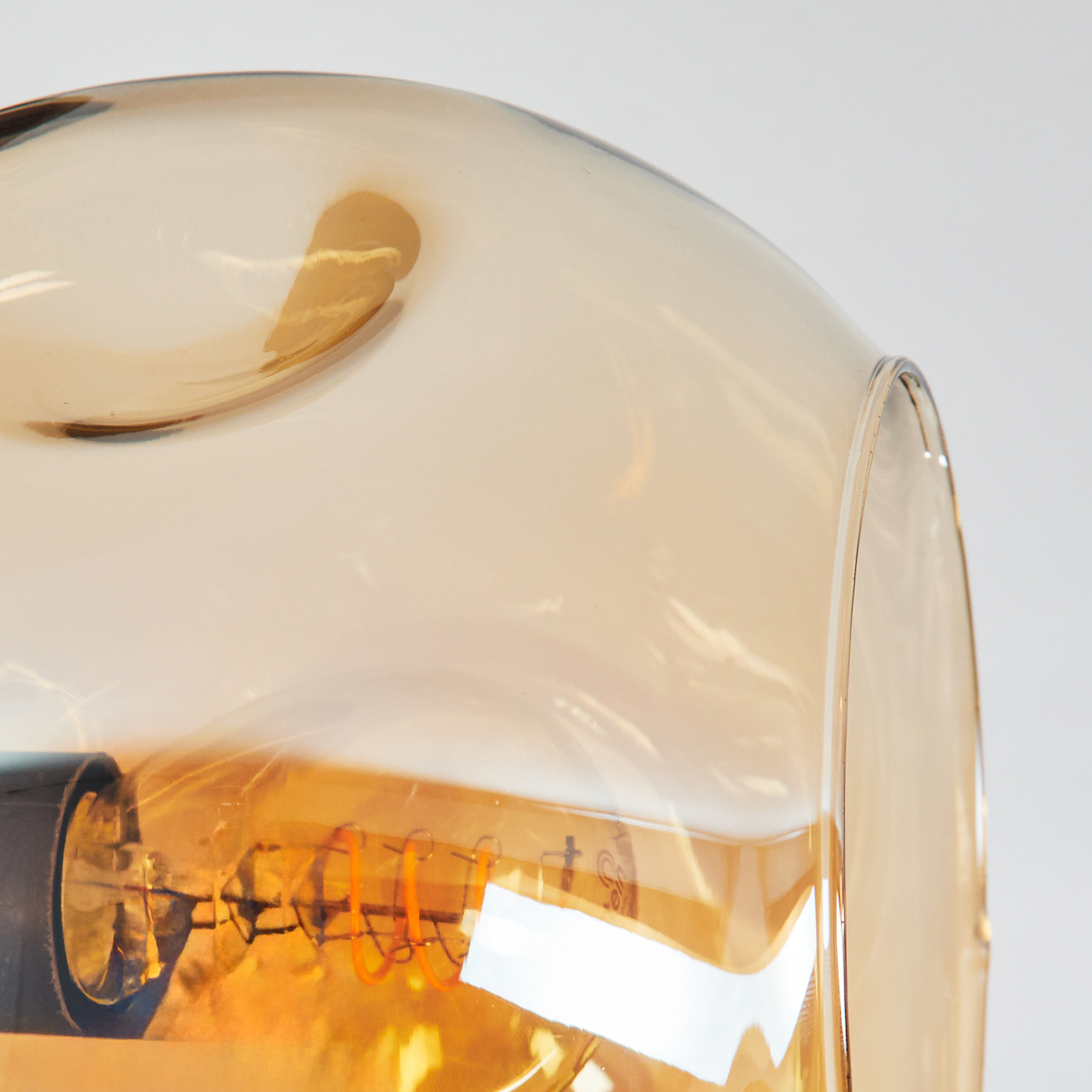Nahaufnahme eines Glasschirms mit sichtbarer Glühbirne. Das Glas ist bernsteinfarben und transparent.