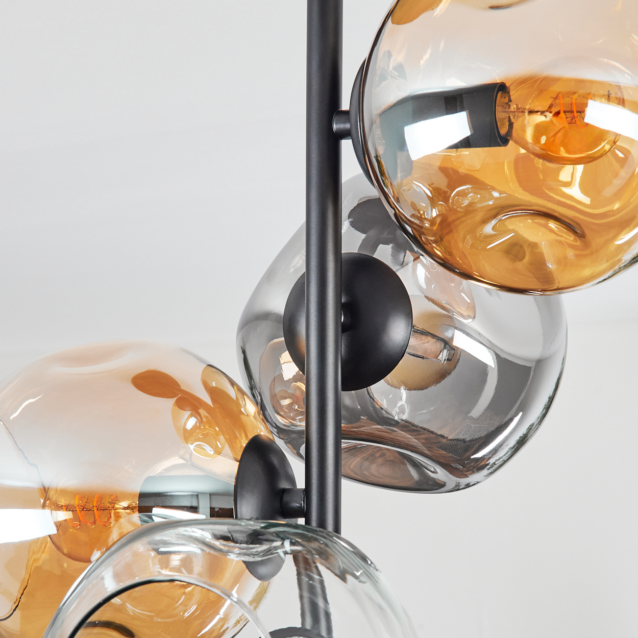Nahaufnahme einer modernen Lampe. Sie hat drei Glaskugeln in Bernstein- und Klarsichtfarben mit schwarzen Metallstützen. Weißer Hintergrund.