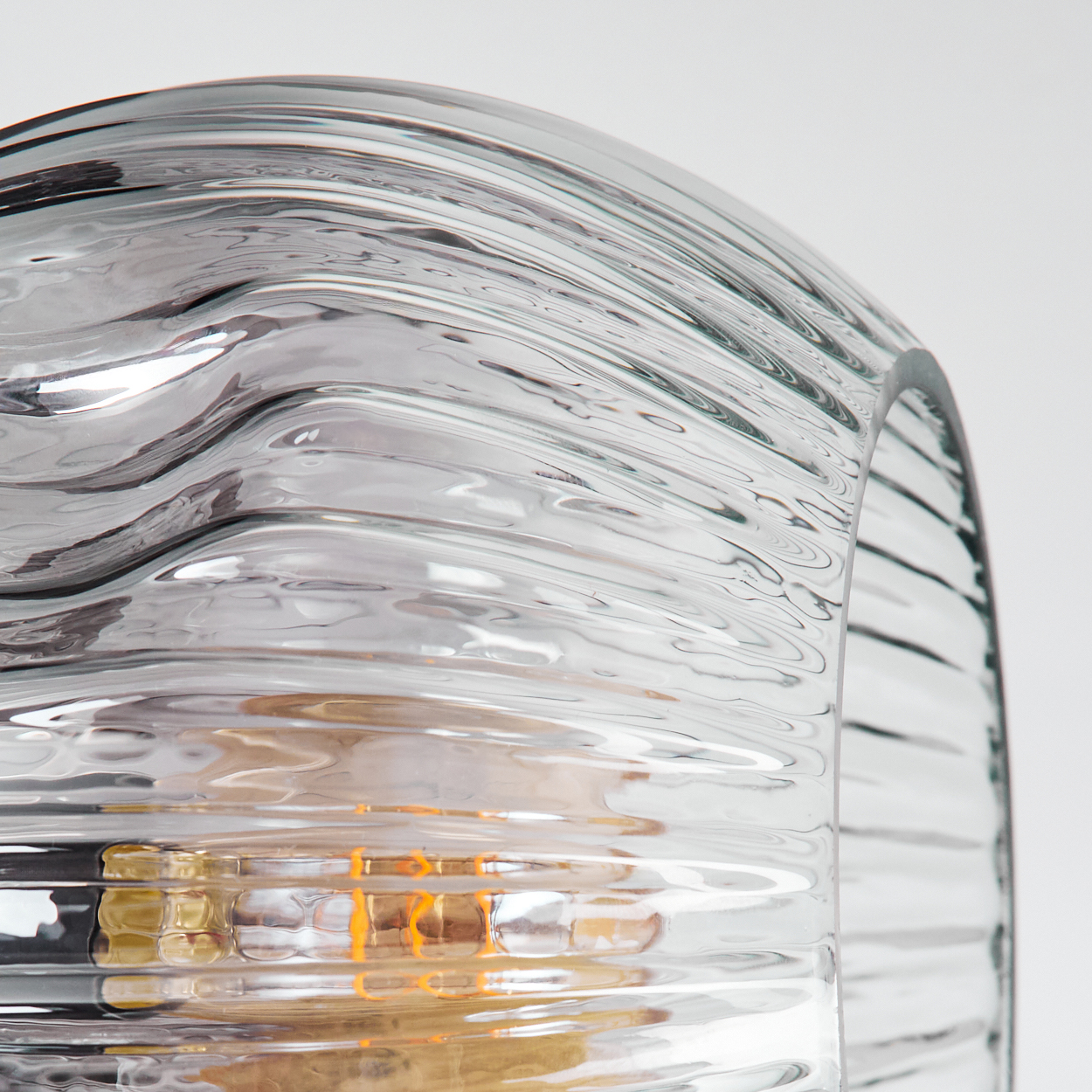 Nahaufnahme einer durchsichtigen Glaslampe mit gewellter Textur. Im Inneren der Lampe ist eine Glühbirne zu sehen, der Hintergrund ist weiß.