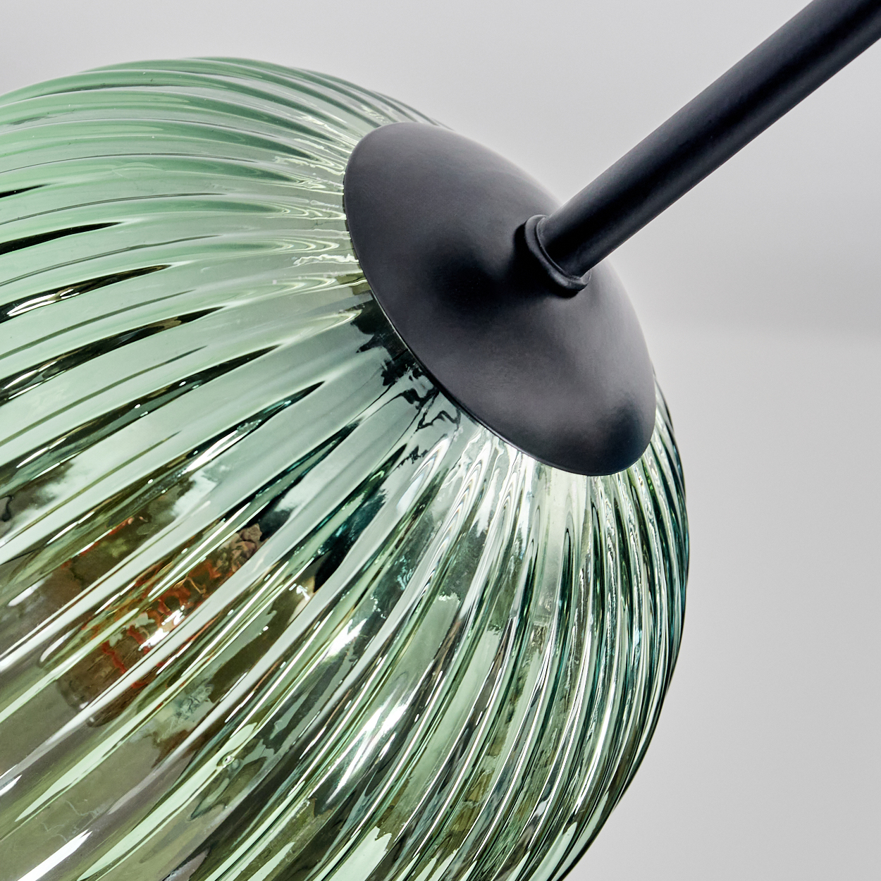 Nahaufnahme eines grünen Glaslampenschirms mit schwarzem Metallarm. Das Glas hat eine gerippte Textur und reflektiert Licht.