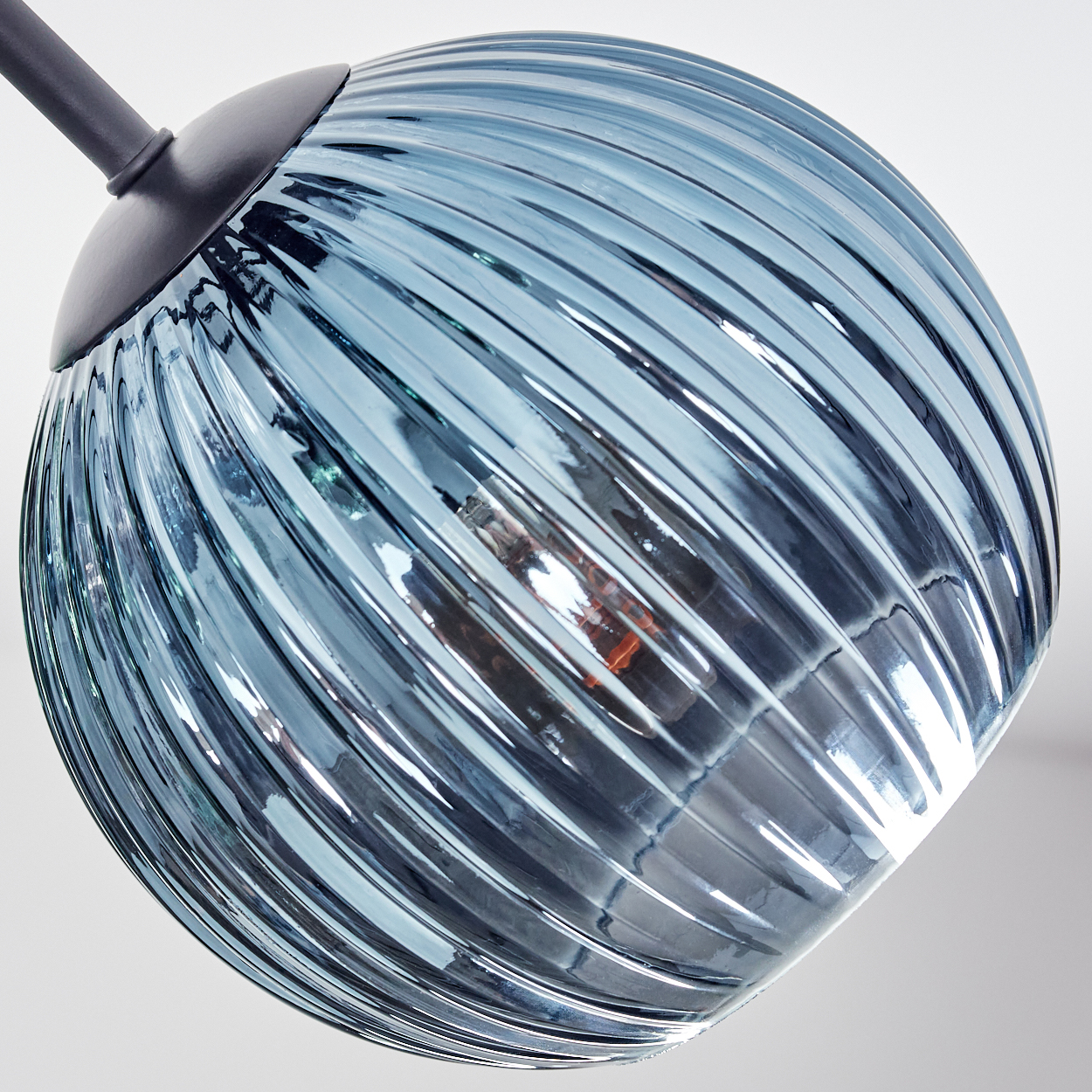 Nahaufnahme einer blauen Glasleuchte. Der kugelförmige Schirm hat ein geripptes Design. Ein dunkler Metallarm stützt den Schirm.