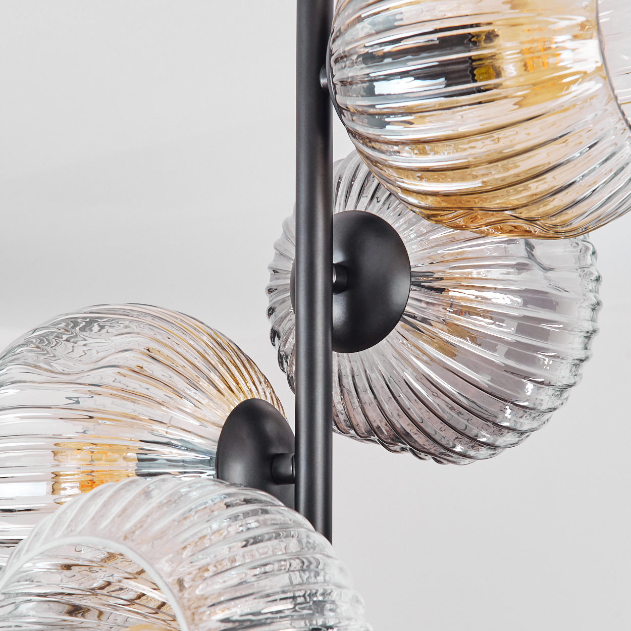 Nahaufnahme einer modernen Lampe mit vier Glasschirmen. Schirme gerippt und kugelförmig, mit bernsteinfarbenem und klarem Glas. Schwarzer Metallrahmen.