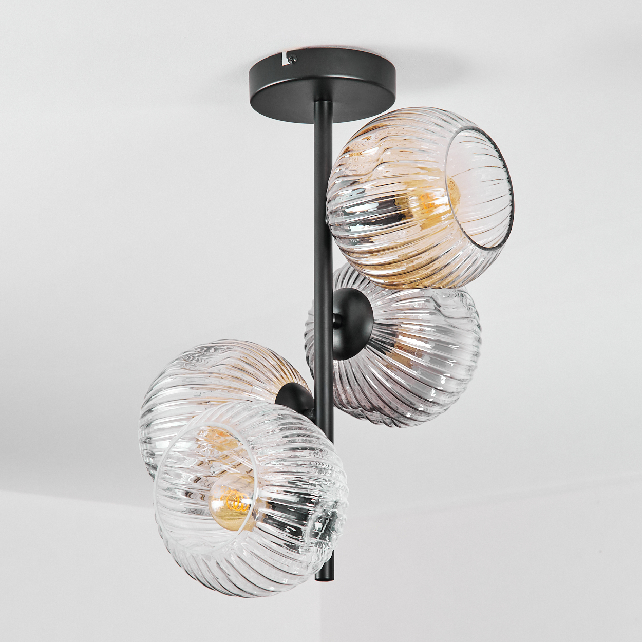 Eine moderne Deckenlampe mit vier Glasschirmen in verschiedenen Farben, die an einem schwarzen Metallrahmen befestigt sind. Weißer Hintergrund.