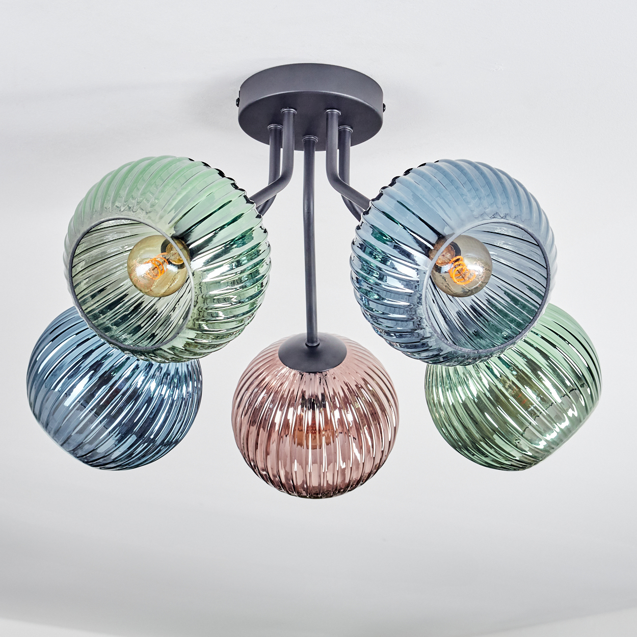 Eine moderne Deckenlampe mit fünf bunten Glasschirmen. Die Schirme sind grün, blau und rosa, mit Glühbirnen im Inneren. Der Hintergrund ist weiß.